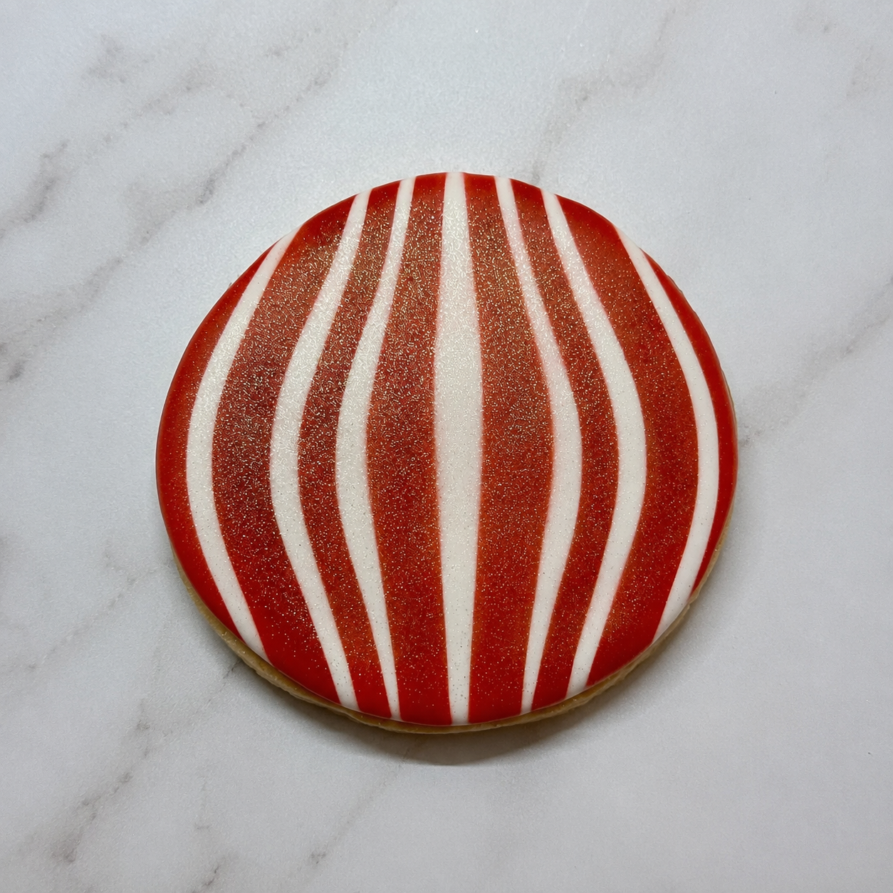 A round sugar cookie airbrushed in red with ourOrnament Lines Cookie Stencil and sprayed with edible glitter