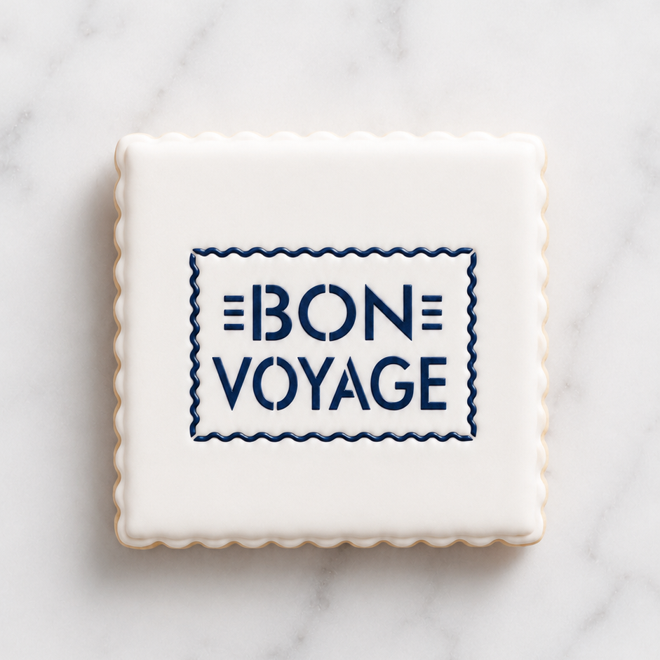 A white cookie with scalloped edges and flooded in white icing, decorated with our Bon Voyage Cookie Stencil in navy blue royal icing