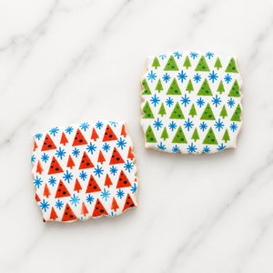 Two white, plaque shaped cookies decorated with our Modern Winter Pattern Stencil Set, one cookie is airbrushed in red and blue and the second is decorated in green and blue
