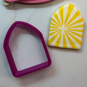 Pointed Arch Cookie Cutter used to make this cookie example that is airbrushed with the Cross Sunburst Stencil in yellow, all placed on a marble counter