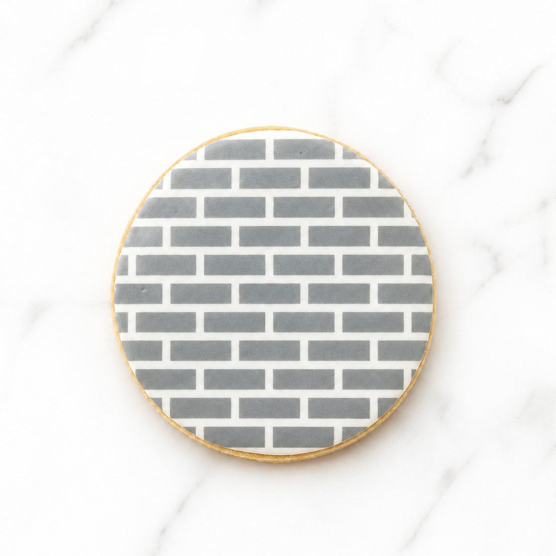 A round sugar cookie airbrushed in gray with our Small Brick Pattern Cookie Stencil