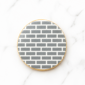 A round sugar cookie airbrushed in gray with our Small Brick Pattern Cookie Stencil