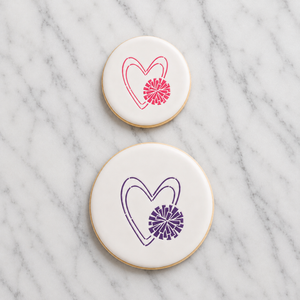 Two white round sugar cookies on a marble countertop, the small cookie decorated with the Cheer Love Cookie Stencil in dark pink royal icing and the large cookie decorated with the same stencil in dark purple royal icing