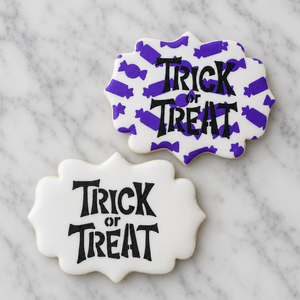 Two white, plaque shaped Halloween sugar cookies decorated with the Tricky Trick or Treat Cookie Stencil in black royal icing and one of the cookies also is stenciled with the Candy Pattern in purple. Both cookies shown on a Carrara Marble counter, BakeArt Stencils