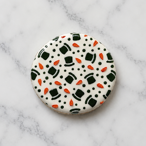 A round cookie, flooded in white icing and decorated with the Melted Snowmen Cookie Stencil Set in black and orange