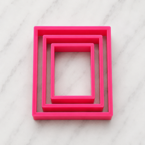 Three sizes of our Rectangle Cookie Cutter in pink food-safe plastic showing nested together on a marble counter
