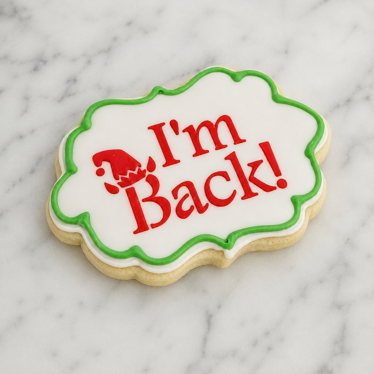 A plaque shaped, white cookie decorated with our I'm Back Elf Cookie Stencil  in red royal icing and piped with a green icing border
