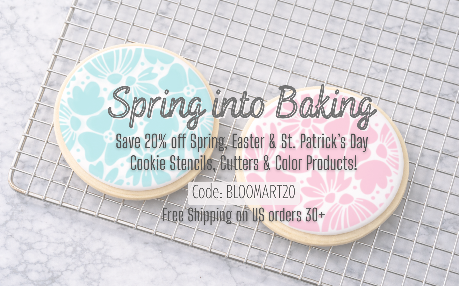Two sugar cookies decorated with floral stencils airbrushed in pink and blue on a cooling rack, featuring the Spring Sale to save 20% off stencils, cutter and color products.