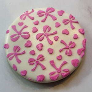 Love-a-Bow Cookie Stencil decorated in pink royal icing on a circle sugar cookie.