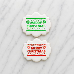 Two white, plaque shaped cookie decorated with our Knitted Merry Christmas Cookie Stencil with one in red and one in green, both shown on a marble counter