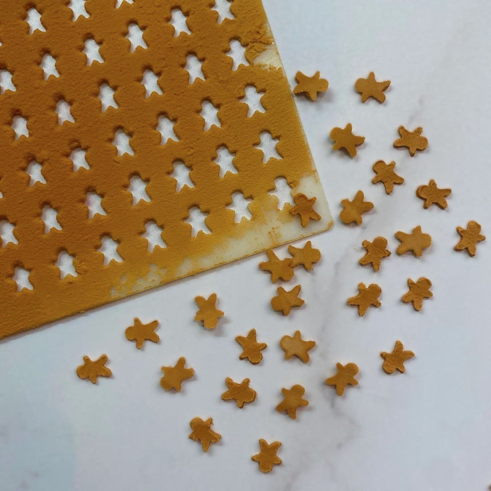 Gingerbread Man Sprinkles made in brown royal icing with this sprinkle stencil and shown on a marble countertop