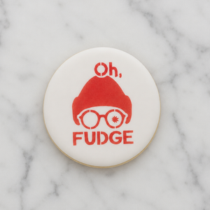 A white, round cookie decorated with the Oh Fudge Cookie Stencil in red and shown on a marble counter