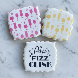 Three plaque shaped cookies, all flooded in white icing. Two are  decorated with our Bar Glasses Cookie Stencil in pink and yellow and one is decorated with our Pop Fizz Clink Stencil in black royal icing