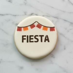 A round sugar cookie flooded in white and decorated with our Fiesta Cookie Stencil in black royal icing and our Fiesta Flags Stencil in red and orange