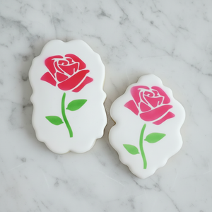 Two plaque shaped cookies, flooded in white icing and decorated with our Rose on Stem Cookie Stencil, one with red petals and a green stem and one with pink petals and a green stem