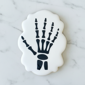 Skeleton Hand Cookie Stencil decorated in black royal icing on a white, plaque shaped sugar cookie.