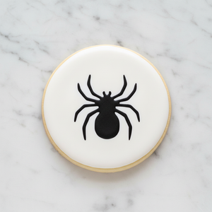 A white round sugar cookie decorate with our Spider Cookie Stencil in black royal icing, laying on marble counter, BakeArt Stencils