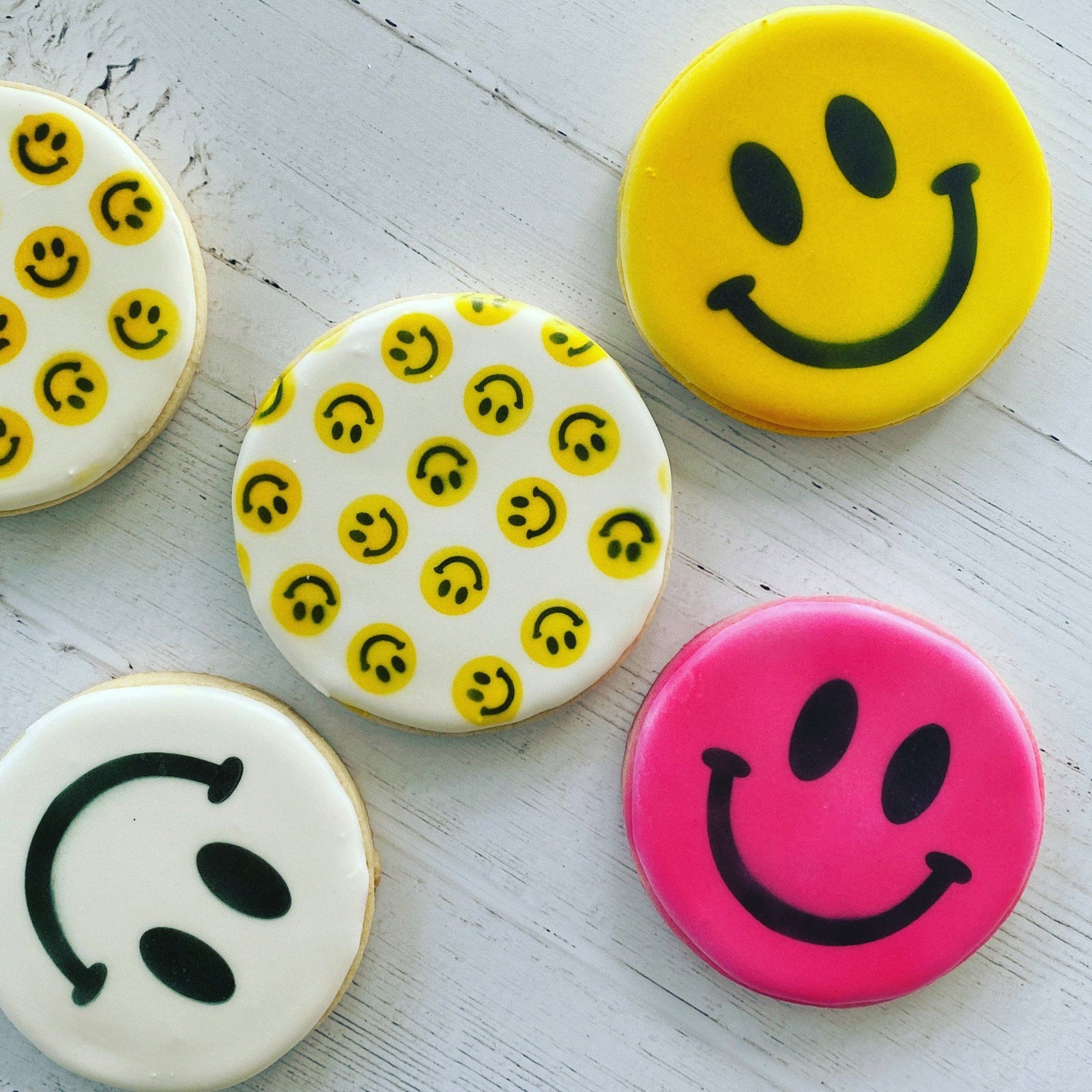 Several round cookies decorated with our Happy Faces Pattern Stencil Set in yellow and black, and also shown with white, yellow and pink cookies made with our Smiley Faces Stencil.