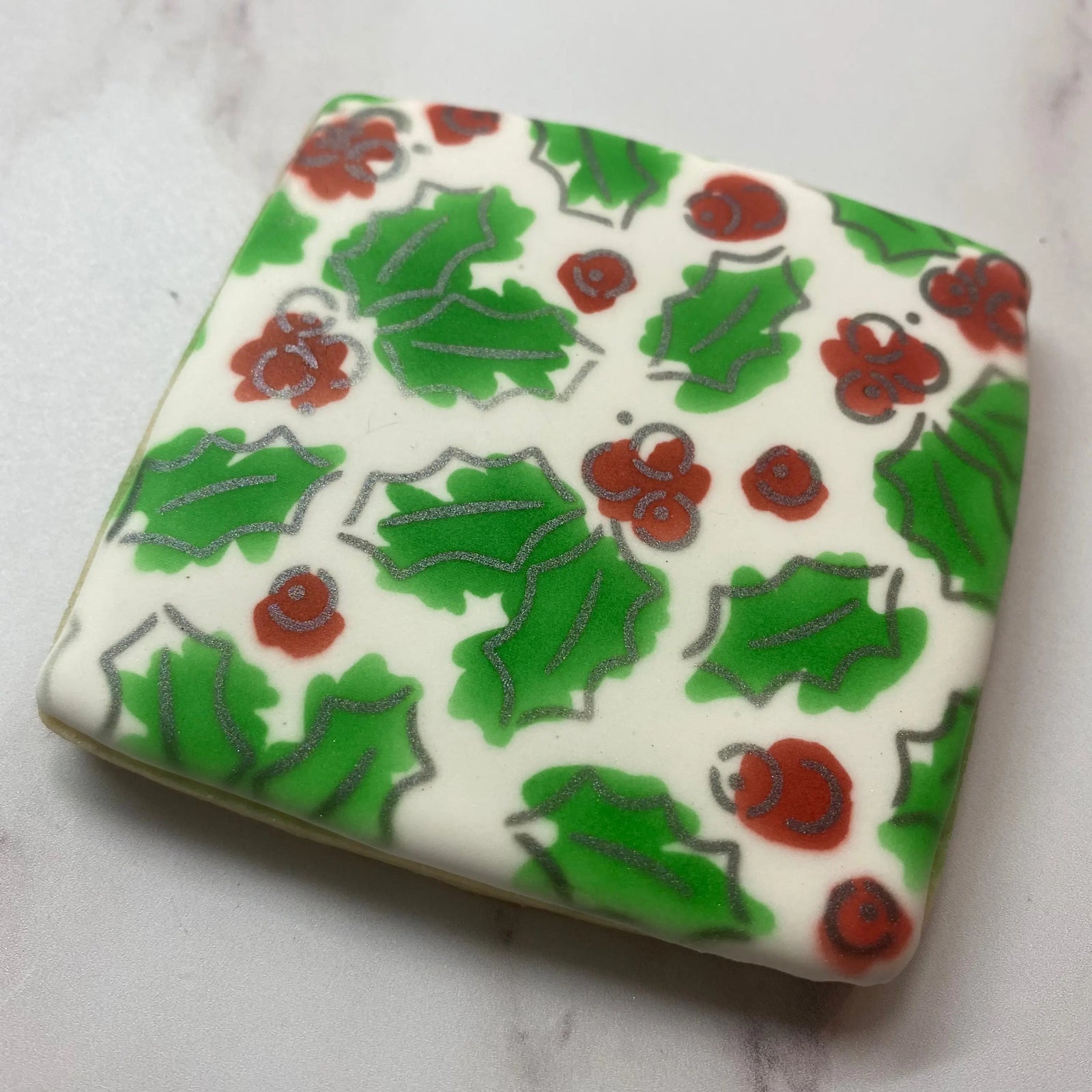 Holiday Holly Cookie Stencil Set airbrushed in red green and sparkly silver onto a square shaped sugar cookie